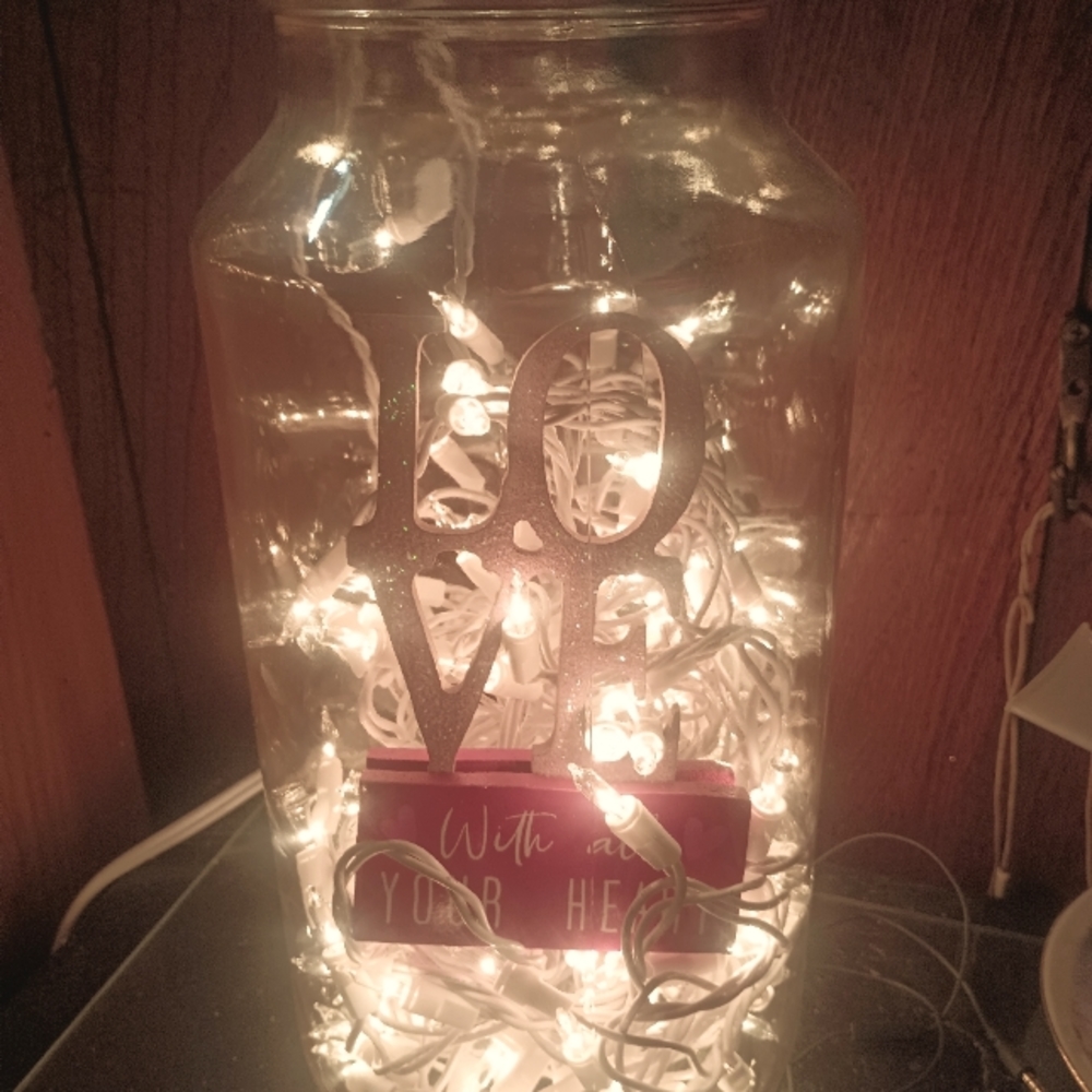 Jar filled with white lights and a Valentine sign that says love is all you need